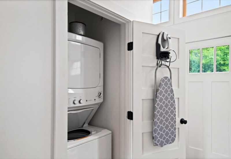 stackable washer and dryer inside a closet with iron and ironing board hanging on the door