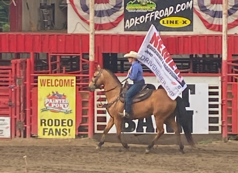 cowgirl riding a horse and holding a flag at the Painted Pony Rodeo